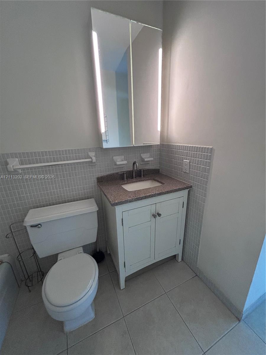 Bathroom featuring a vanity with stone-finish countertop, under-mount sink, white cabinetry, integrated medicine cabinet with built-in vertical lighting, and tiled wall surround
