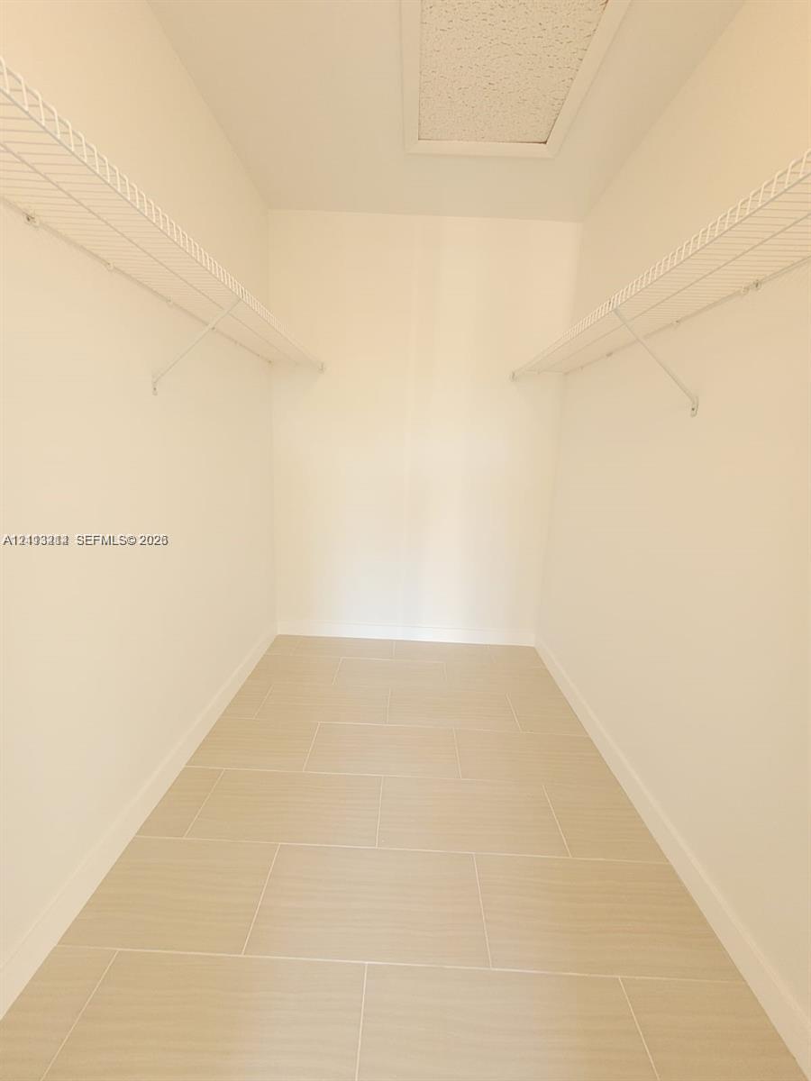 Walk-in storage space featuring large-format ceramic tile flooring, dual-level white wire shelving, and an attic access panel