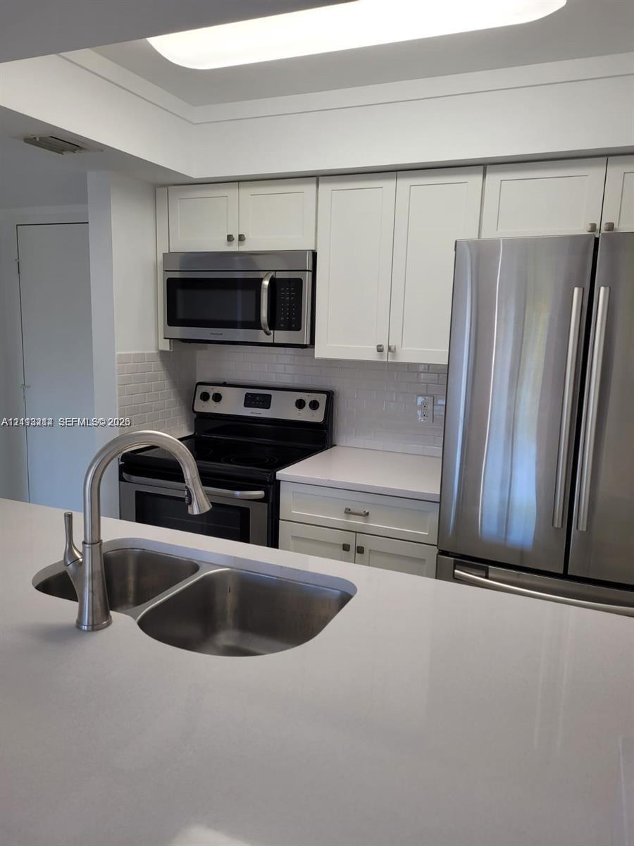 Kitchen featuring white cabinetry, solid-surface countertops, subway tile backsplash, stainless steel appliances, and a double-basin sink with a pull-down faucet