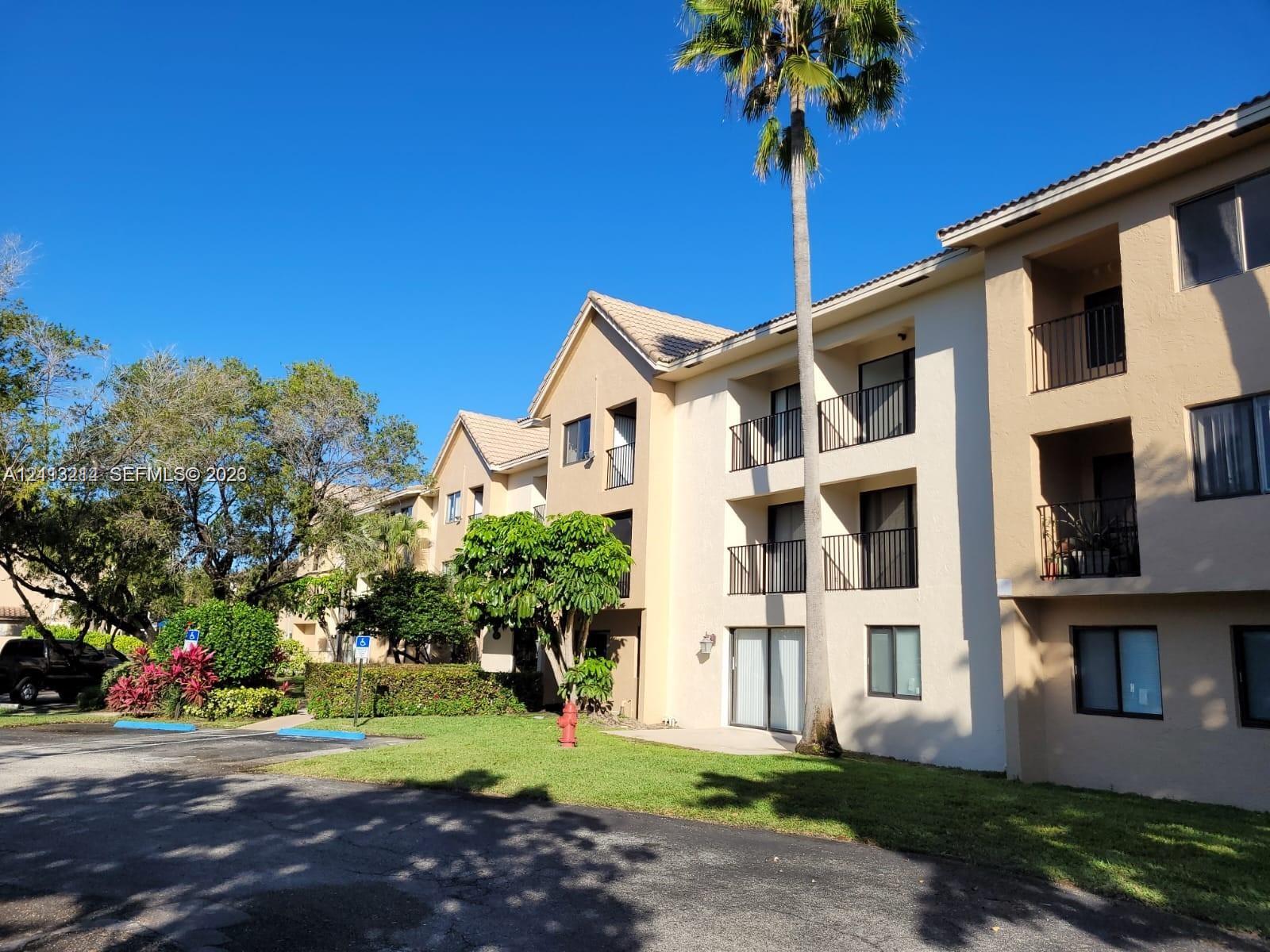 Multi-story exterior featuring a light-toned stucco facade, tiled roof, private balconies with metal railings, and mature landscaping