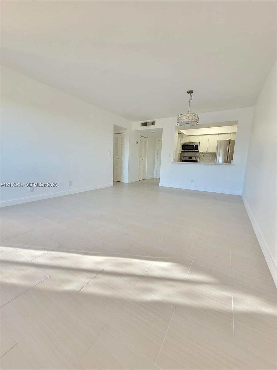 Open living area featuring neutral-tone ceramic tile flooring, a pass-through kitchen opening, drum-style pendant lighting, and crisp white wall finishes