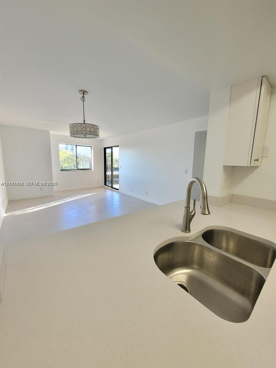 Kitchen featuring a double-basin stainless steel sink, gooseneck faucet, solid-surface countertop, and white cabinetry, complemented by tile flooring and a decorative drum pendant light