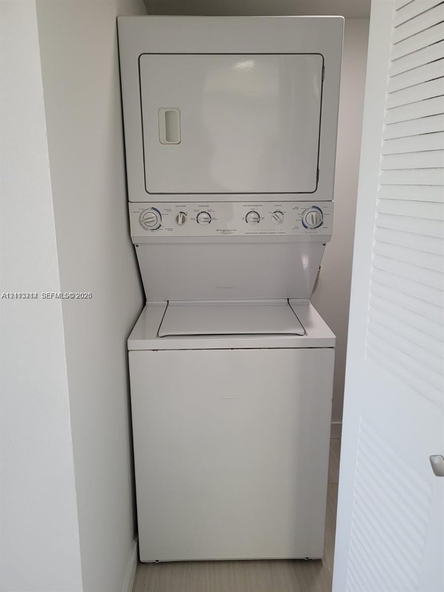Stacked white washer and dryer unit enclosed within a closet with a louvered door