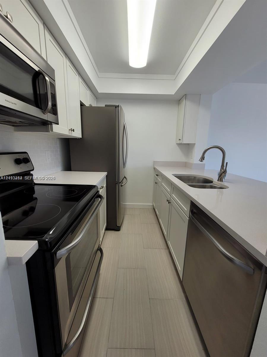 Kitchen featuring white shaker-style cabinetry, neutral stone-finish countertops, stainless steel appliances, a double-basin undermount sink with a gooseneck faucet, and light-toned tile flooring