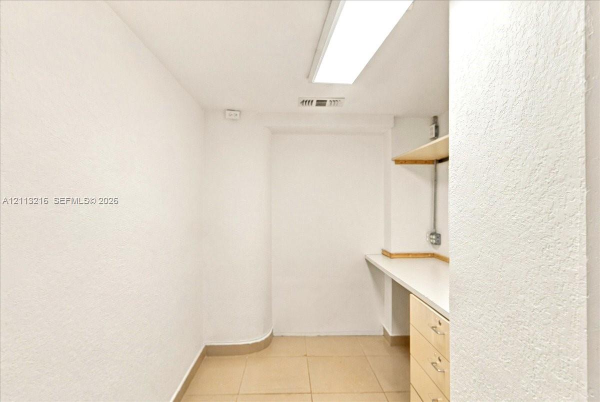 Neutral workspace featuring ceramic tile flooring, built-in cabinetry with a white countertop, and wall-mounted shelving