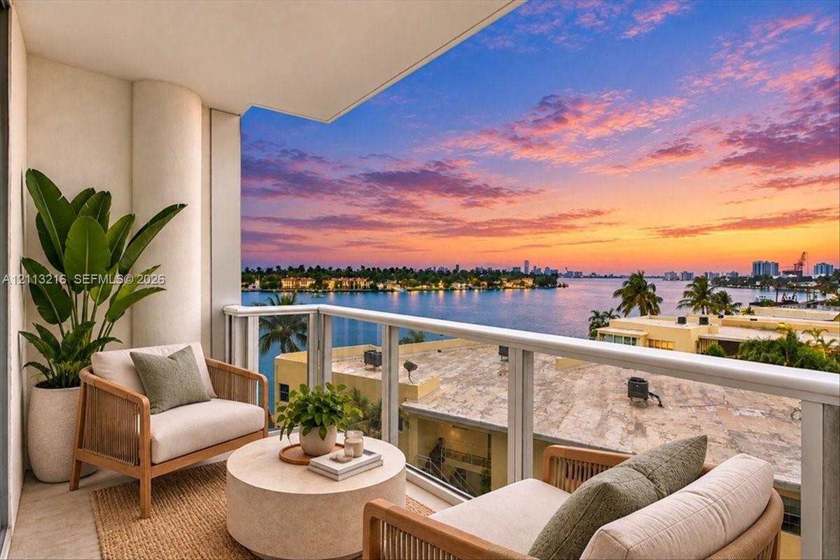Covered balcony featuring neutral stone flooring and a glass-paneled railing with a waterfront backdrop Covered balcony featuring neutral stone flooring and a glass-paneled railing with a waterfront backdrop