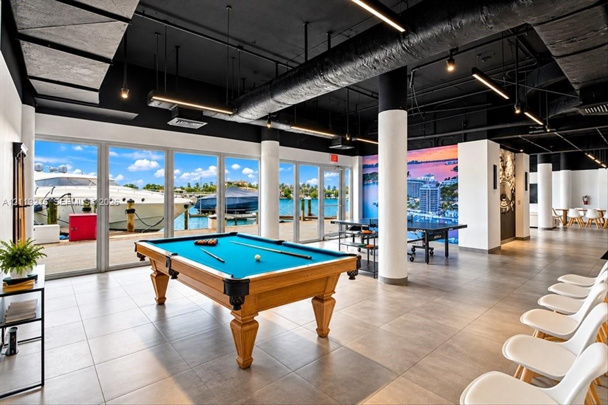Industrial-style common area featuring floor-to-ceiling windows, porcelain tile flooring, exposed ductwork, cylindrical support columns, and marina frontage
