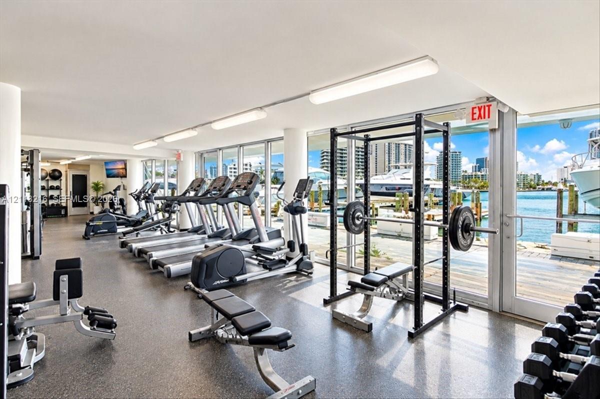 Fitness center featuring floor-to-ceiling windows, waterfront scenery, rubberized flooring, linear lighting, and built-in structural columns