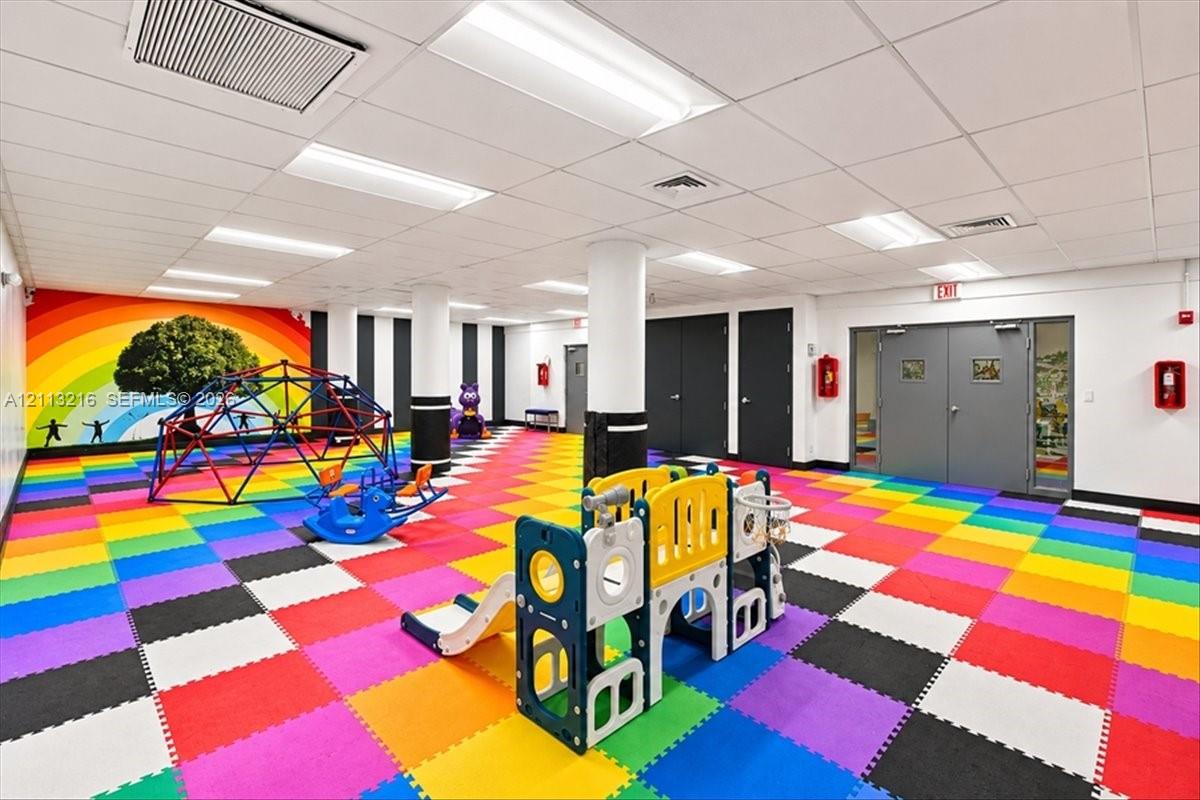Multi-purpose recreation room featuring modular foam tile flooring, a recessed drop ceiling, structural support columns, and double-door entry points
