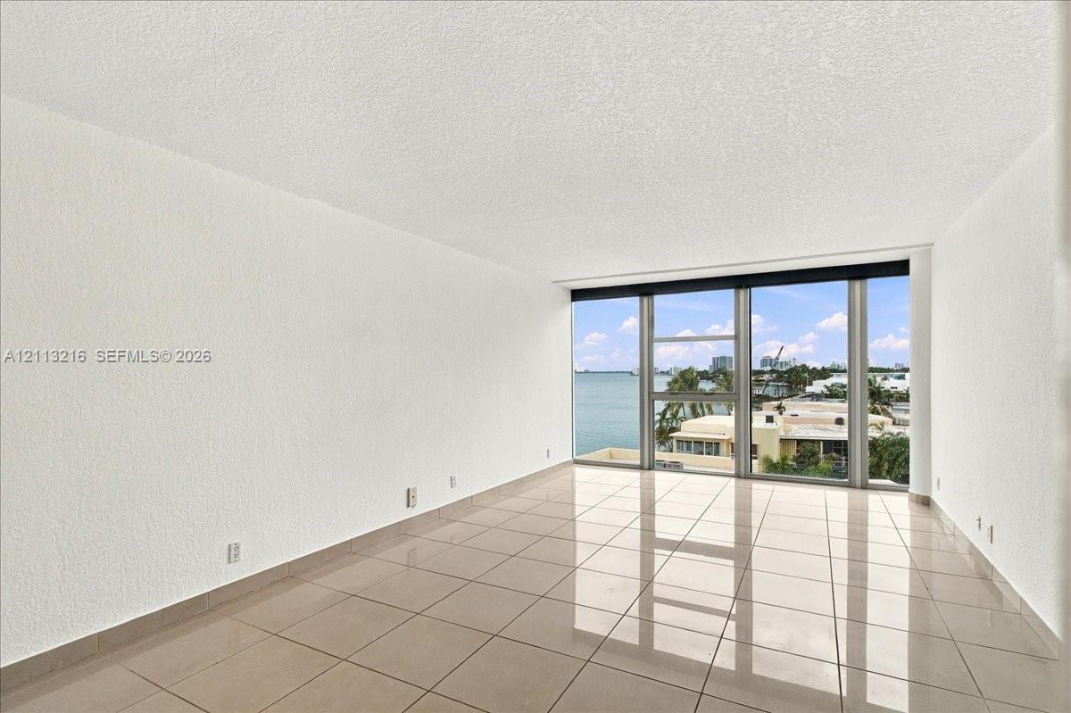 Expansive room featuring polished tile flooring, floor-to-ceiling windows, and water scenery