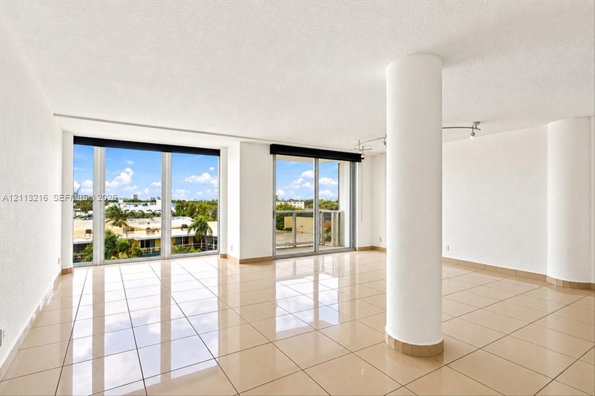 Open-concept interior featuring large-format tile flooring, floor-to-ceiling windows, a private balcony, structural columns, and recessed track lighting