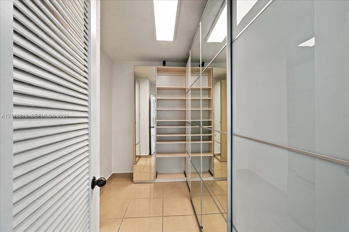Storage area featuring built-in wooden shelving, full-height mirrored wardrobe doors, tile flooring, and louvered entry door