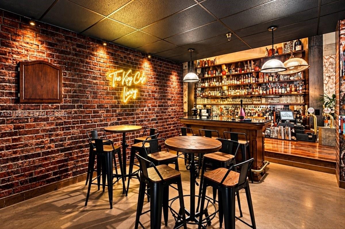 Exposed brick wall with recessed accent lighting, built-in wooden bar, multi-tiered shelving, and dual industrial-style pendant light fixtures