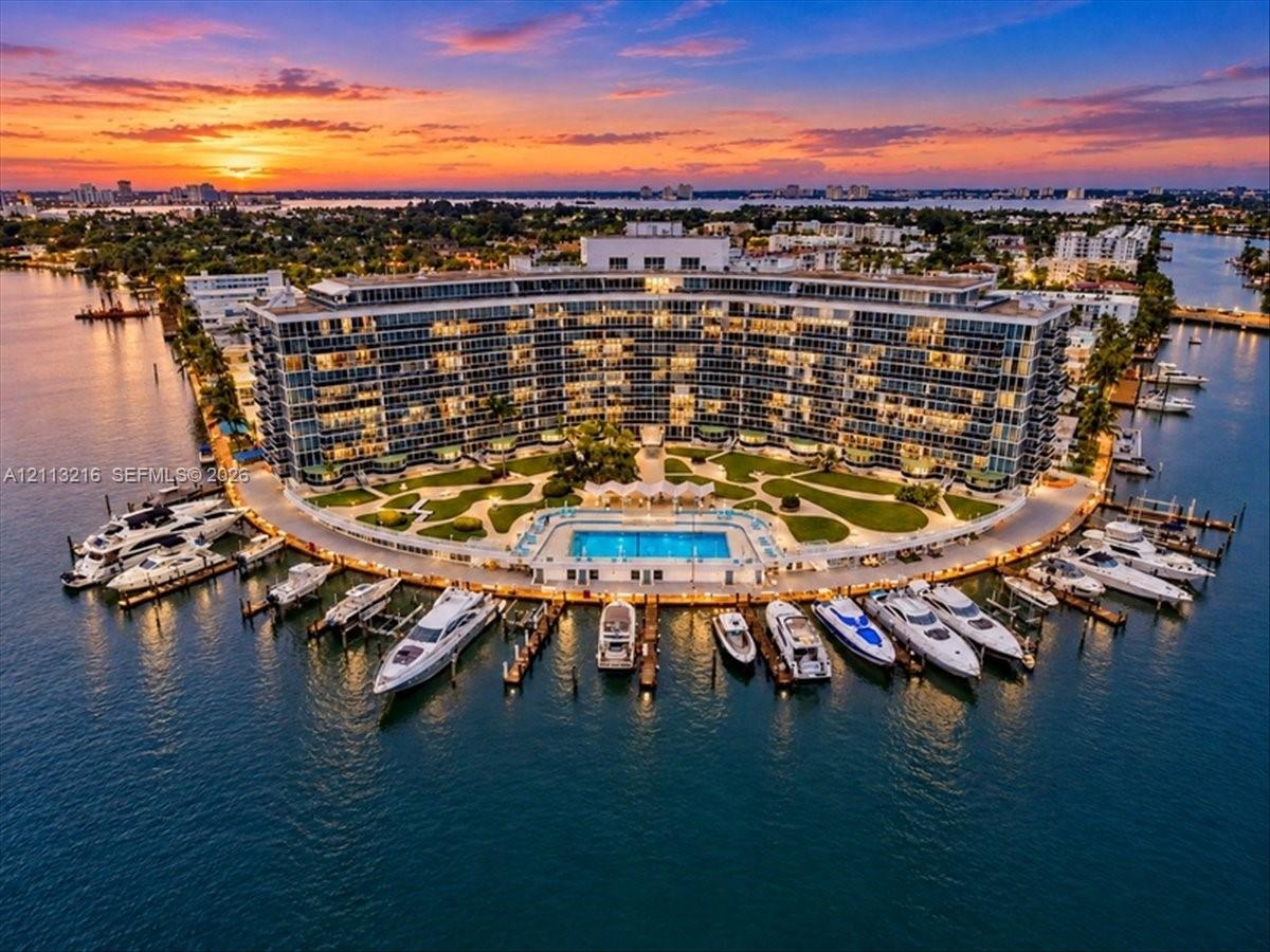 Waterfront multi-story residential structure featuring a private marina, paved boat slips, a perimeter swimming pool, and expansive manicured grounds
