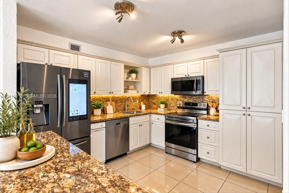 Kitchen featuring white cabinetry, stone countertops, integrated under-cabinet lighting, tile flooring, and stainless steel appliances