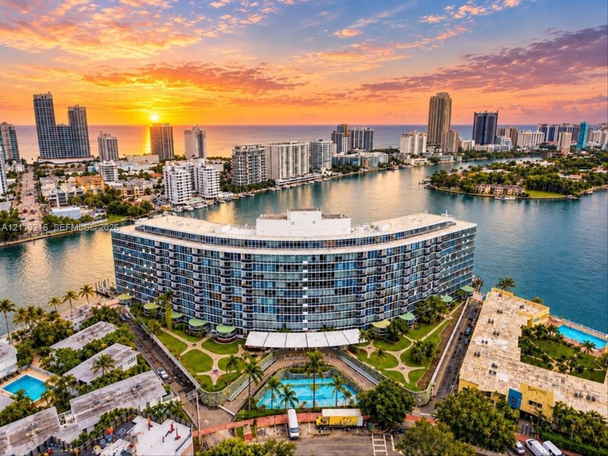 Curved high-rise residential architecture featuring floor-to-ceiling glass paneling, a landscaped courtyard, an outdoor swimming pool, and a waterfront position