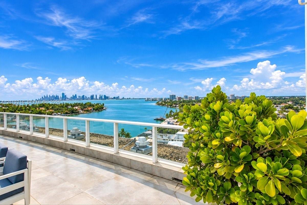 Expansive terrace featuring light-toned tile flooring, glass panel railings, and a wide-reaching water and cityscape backdrop
