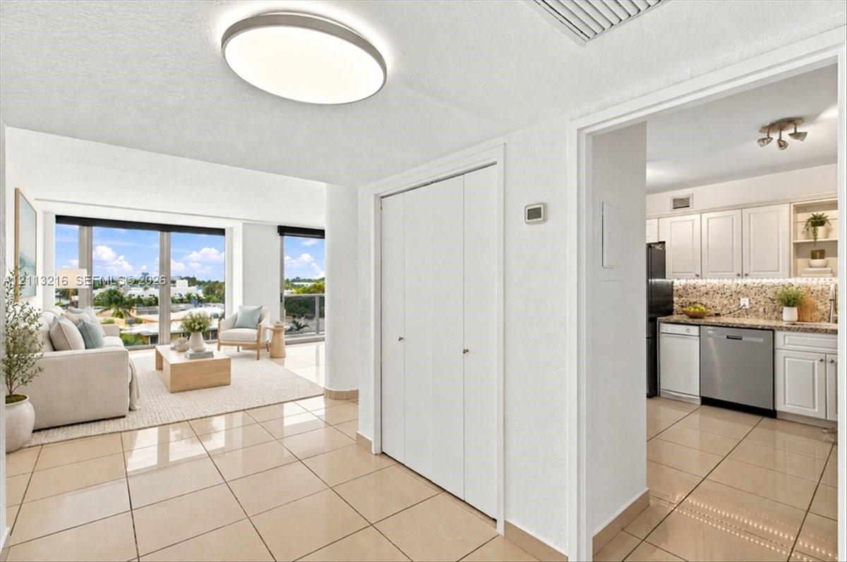 Neutral-toned tile flooring, floor-to-ceiling windows, built-in dual-door closet, and kitchen featuring white cabinetry with stainless steel appliances Neutral-toned tile flooring, floor-to-ceiling windows, built-in dual-door closet, and kitchen featuring white cabinetry with stainless steel appliances