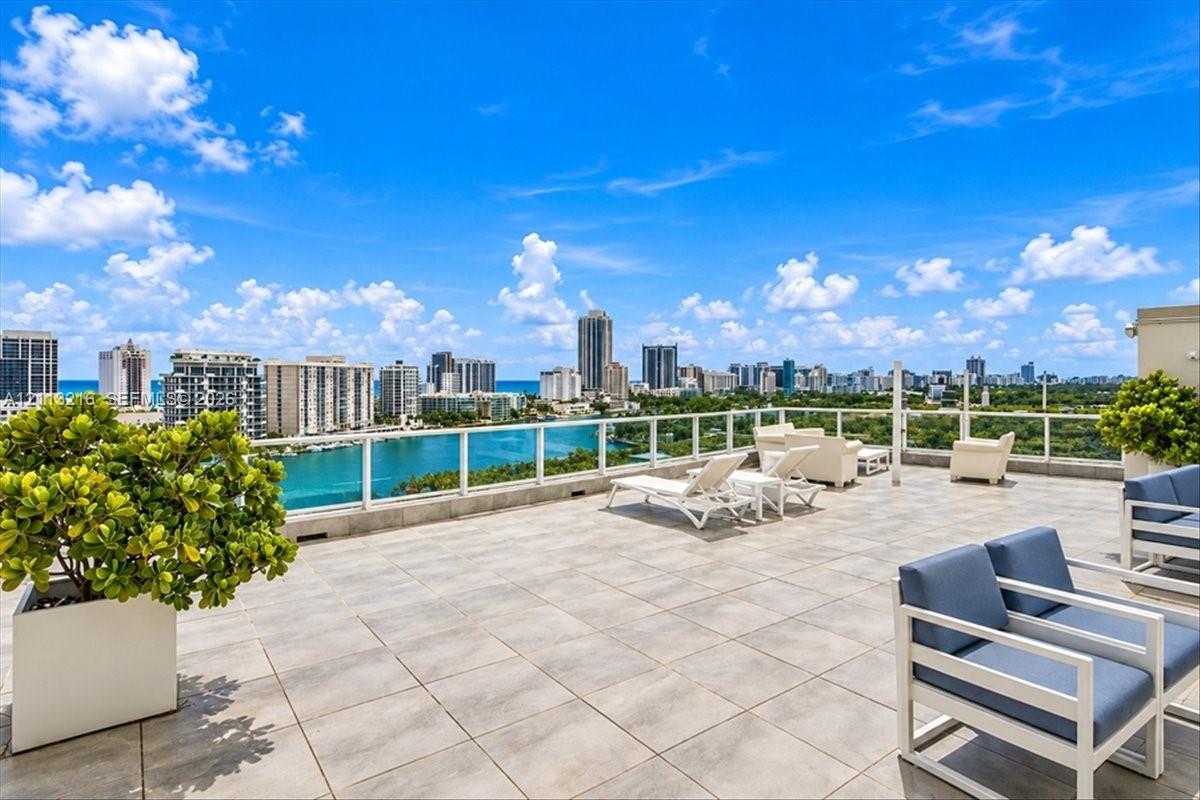 Expansive rooftop terrace featuring large-format stone tile flooring, clear glass railings, and panoramic skyline and coastal water vistas