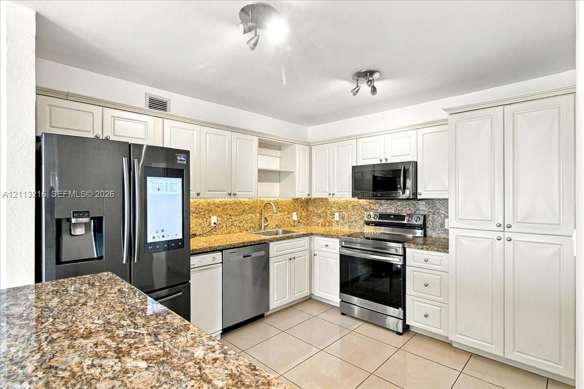 Kitchen featuring white cabinetry, stone-finish countertops, stainless steel appliances, and tile flooring