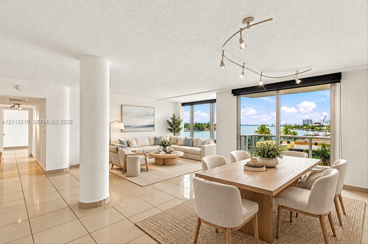 Open floor plan featuring tile flooring, structural pillar, adjustable multi-head track lighting, and floor-to-ceiling glass sliding doors with water scenery