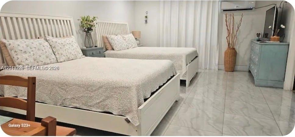 Neutral-toned room featuring large-format stone-finish tile flooring, wall-mounted climate control unit, and floor-to-ceiling drapery