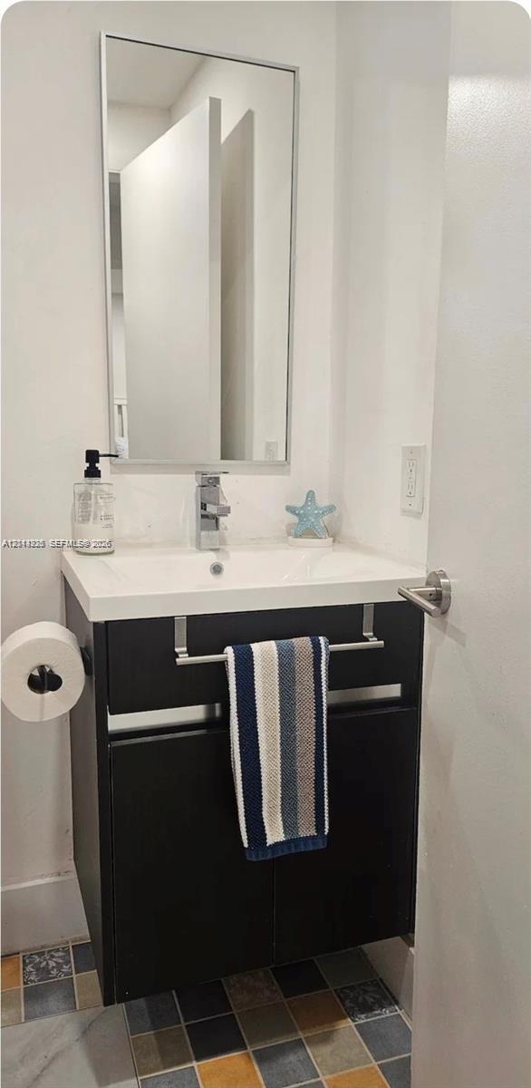 Dark-toned vanity with a rectangular sink, polished chrome faucet, rectangular wall-mounted mirror, and multi-colored square tile flooring