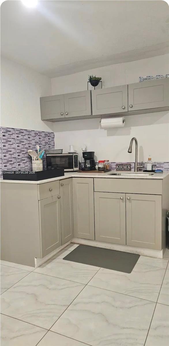 Kitchenette featuring light-toned shaker-style cabinetry, a stone-composite countertop, a high-arc faucet with an undermount sink, a mosaic-tiled backsplash, and large-format porcelain tile flooring