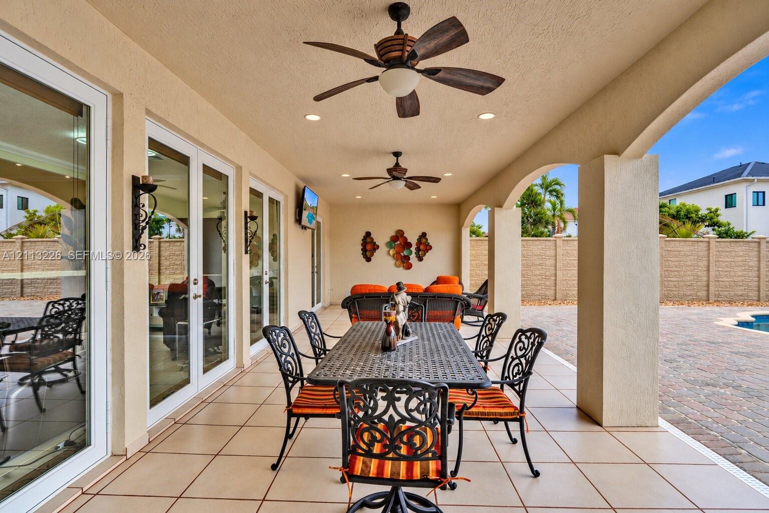 Covered patio featuring tiled flooring, recessed lighting, dual ceiling fans, arched support columns, and multi-panel sliding glass doors