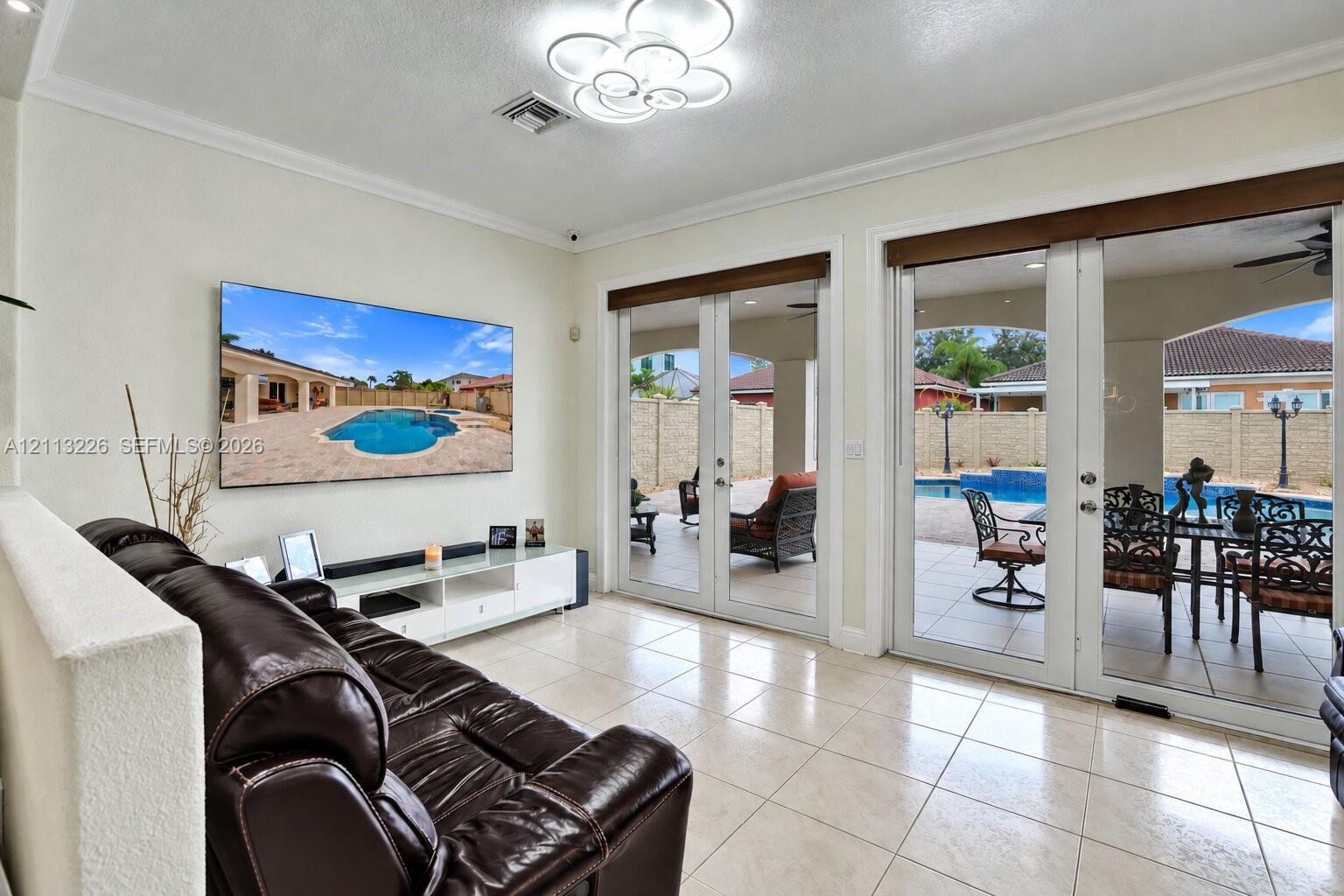 Neutral tile flooring, multi-light contemporary ceiling fixture, and dual sets of glass-paned double doors providing outdoor access