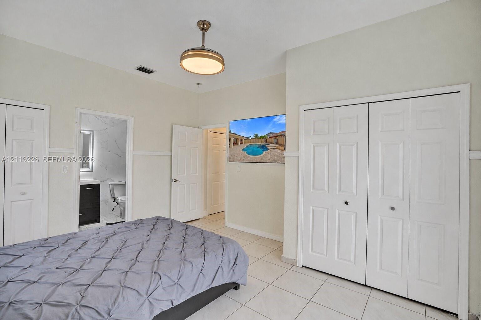 Neutral-toned interior featuring ceramic tile flooring, dual sets of bi-fold closet doors, a contemporary pendant light fixture, and crown molding detail