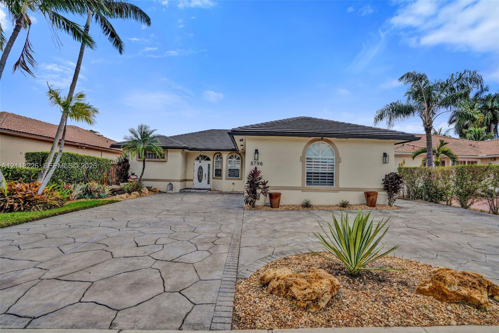 Single-story residence featuring a tile roof, light-toned stucco exterior, arched window detailing, an ornate glass-panel front door, and a decorative stone-patterned driveway
