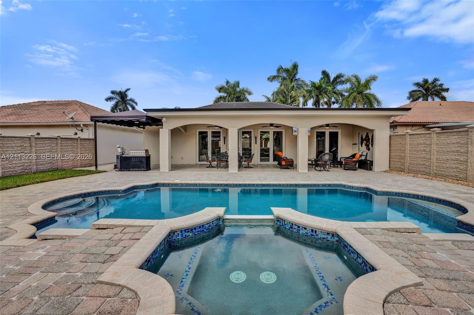 Backyard featuring an inground pool with an integrated spa, paved pool deck, covered patio with arched supports, and perimeter masonry fencing Backyard featuring an inground pool with an integrated spa, paved pool deck, covered patio with arched supports, and perimeter masonry fencing