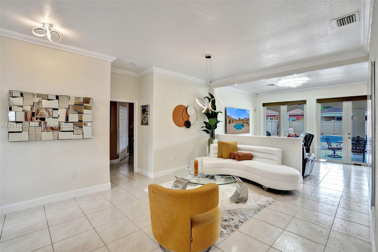 Neutral-toned interior featuring large-format ceramic tile flooring, crown molding, modern dual-ring ceiling-mounted light fixtures, and glass-paneled double doors leading to the exterior