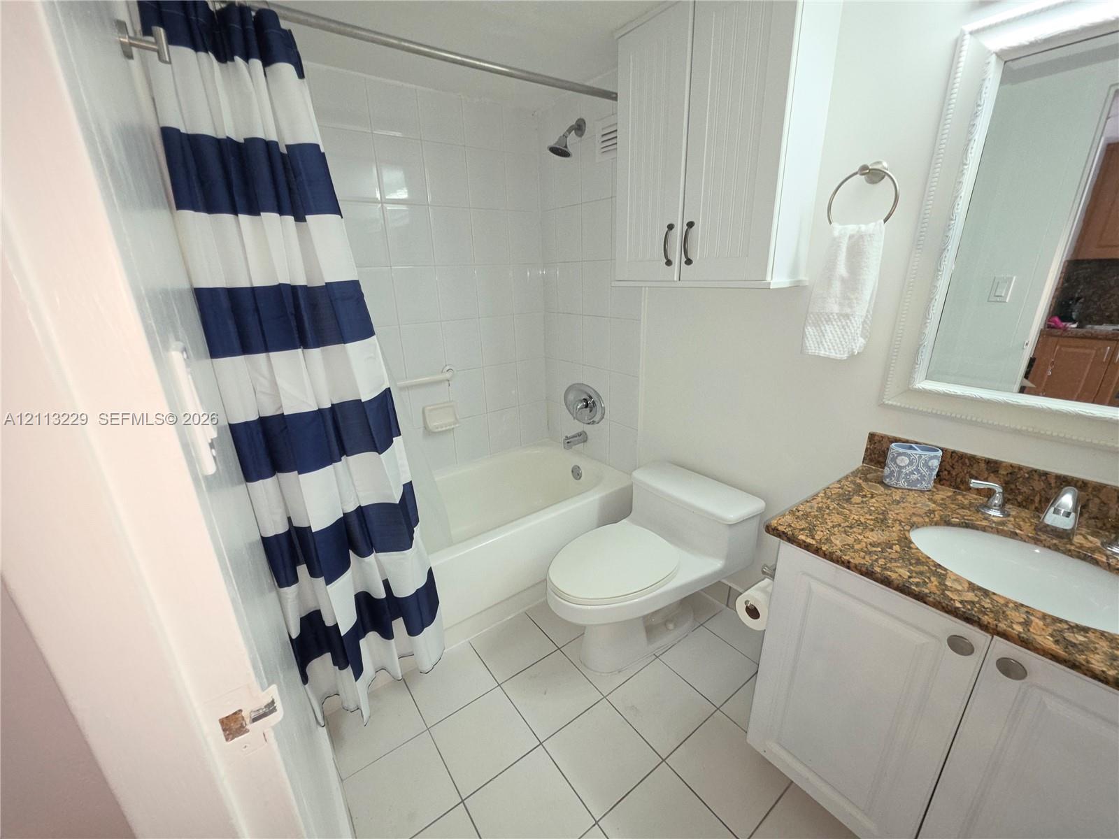 Bathroom featuring a white vanity cabinet with stone-finish countertop, white tile flooring, wall-mounted storage cabinetry, and a tub with tile surround