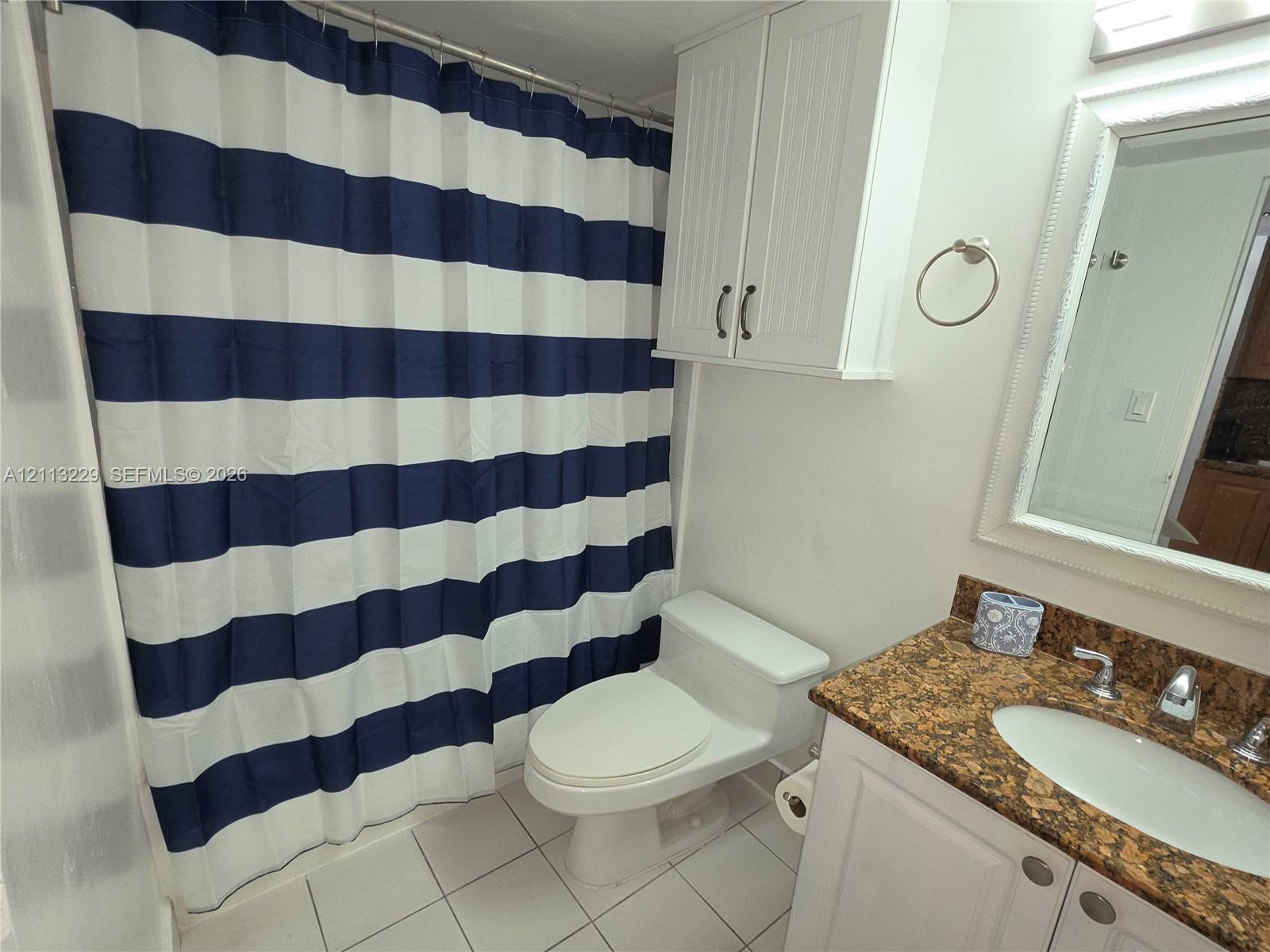 Bathroom featuring white wall-mounted cabinetry, a stone-surfaced vanity with an integrated oval sink, a wall-mounted mirror with decorative molding, and tile flooring