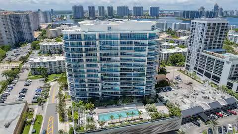 High-rise residential building featuring floor-to-ceiling glass paneling, a multi-level concrete facade, and an elevated outdoor swimming pool with mature palms