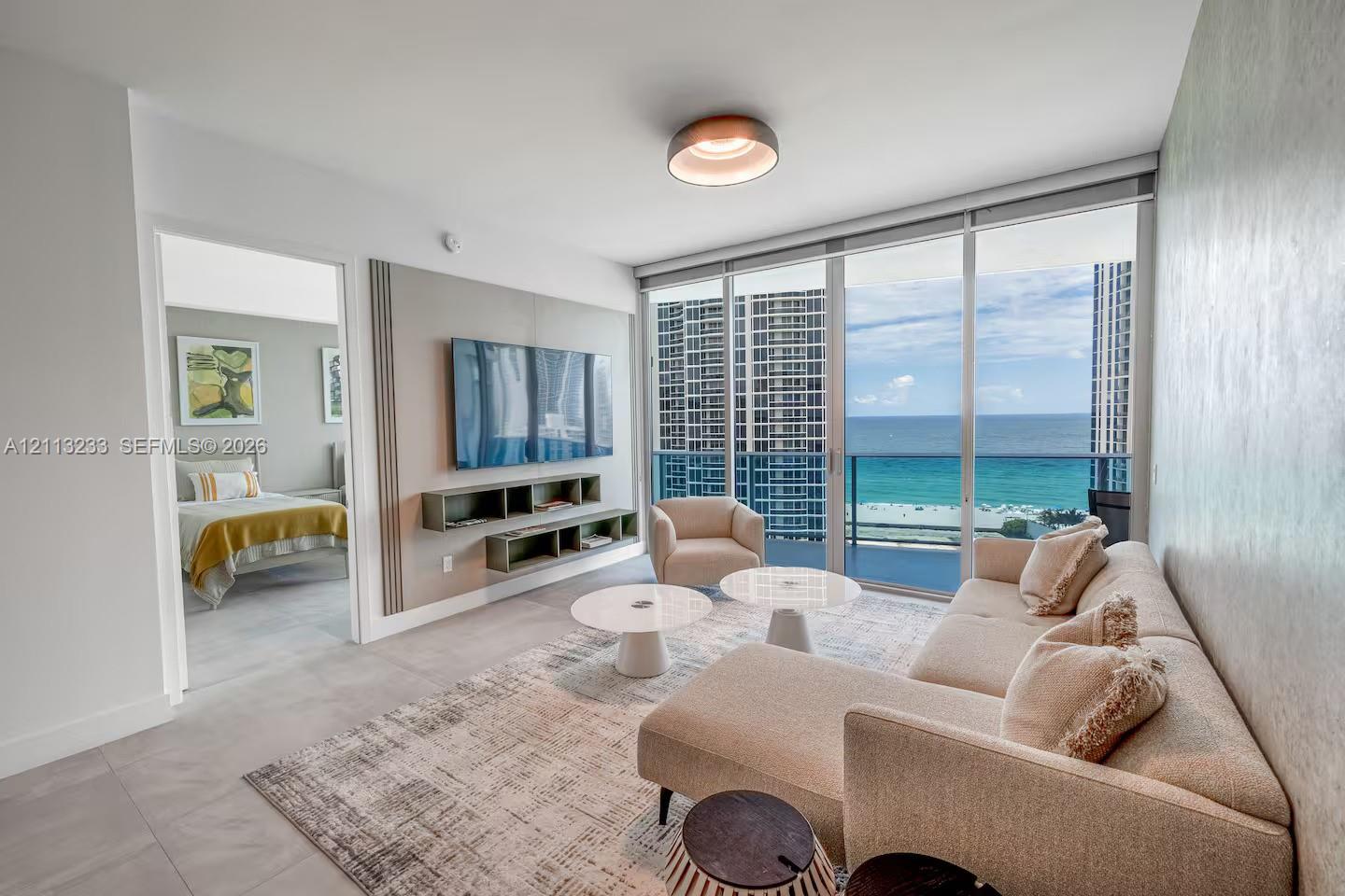 Living space featuring floor-to-ceiling glass sliding doors, custom wall-mounted media shelving, recessed ceiling lighting, and large-format tile flooring