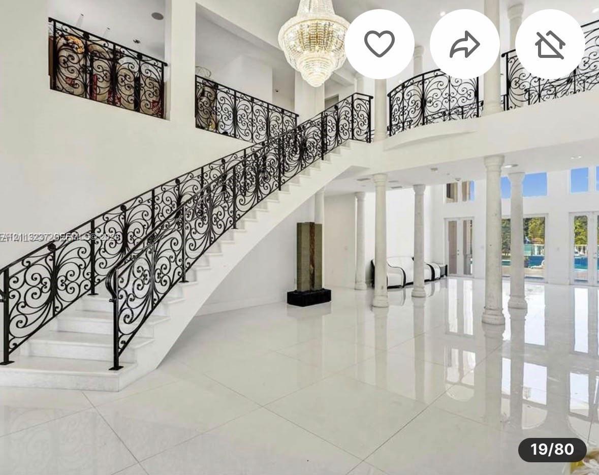 Grand foyer featuring polished tile flooring, decorative wrought-iron railings, a multi-tiered crystal chandelier, and soaring classical columns