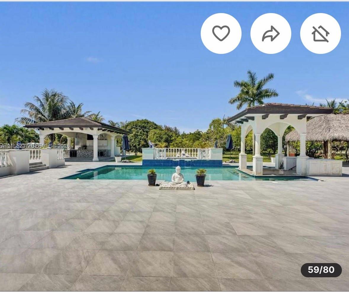 Extensive patio area with large-format tile flooring, rectangular pool, dual covered structures with architectural columns, and a tiered fountain feature