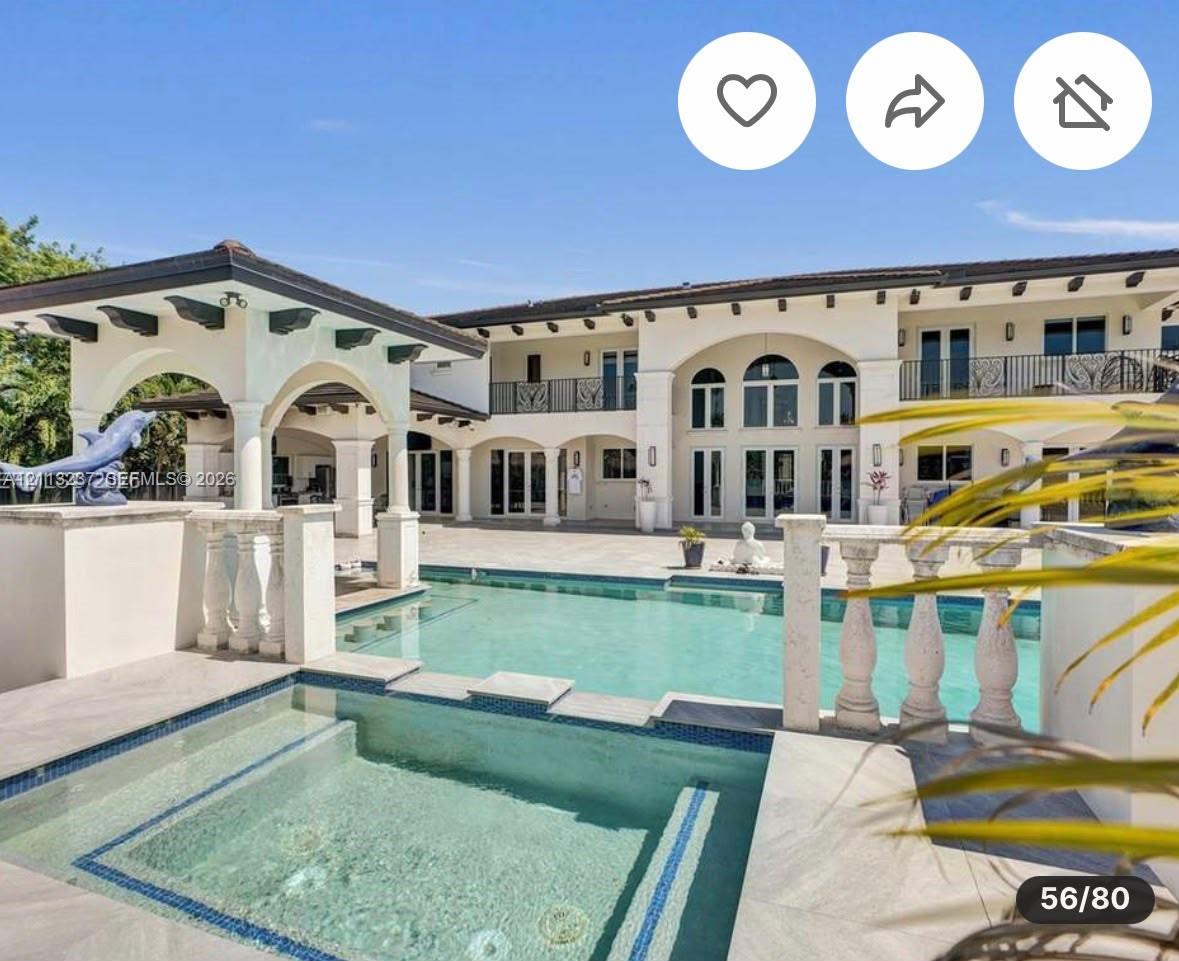 Two-story estate exterior featuring a tiled swimming pool with an integrated spa, stone balustrade railings, a covered patio with decorative support beams, and arched architectural detailing