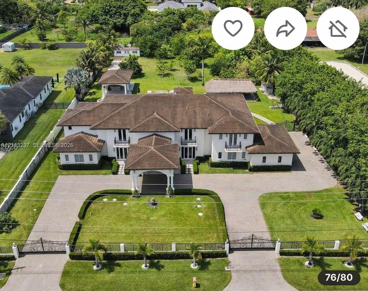 Expansive estate featuring a gated entrance, a paved circular driveway, a porte-cochre, a multi-gabled roofline, and an integrated outdoor pavilion Expansive estate featuring a gated entrance, a paved circular driveway, a porte-cochre, a multi-gabled roofline, and an integrated outdoor pavilion