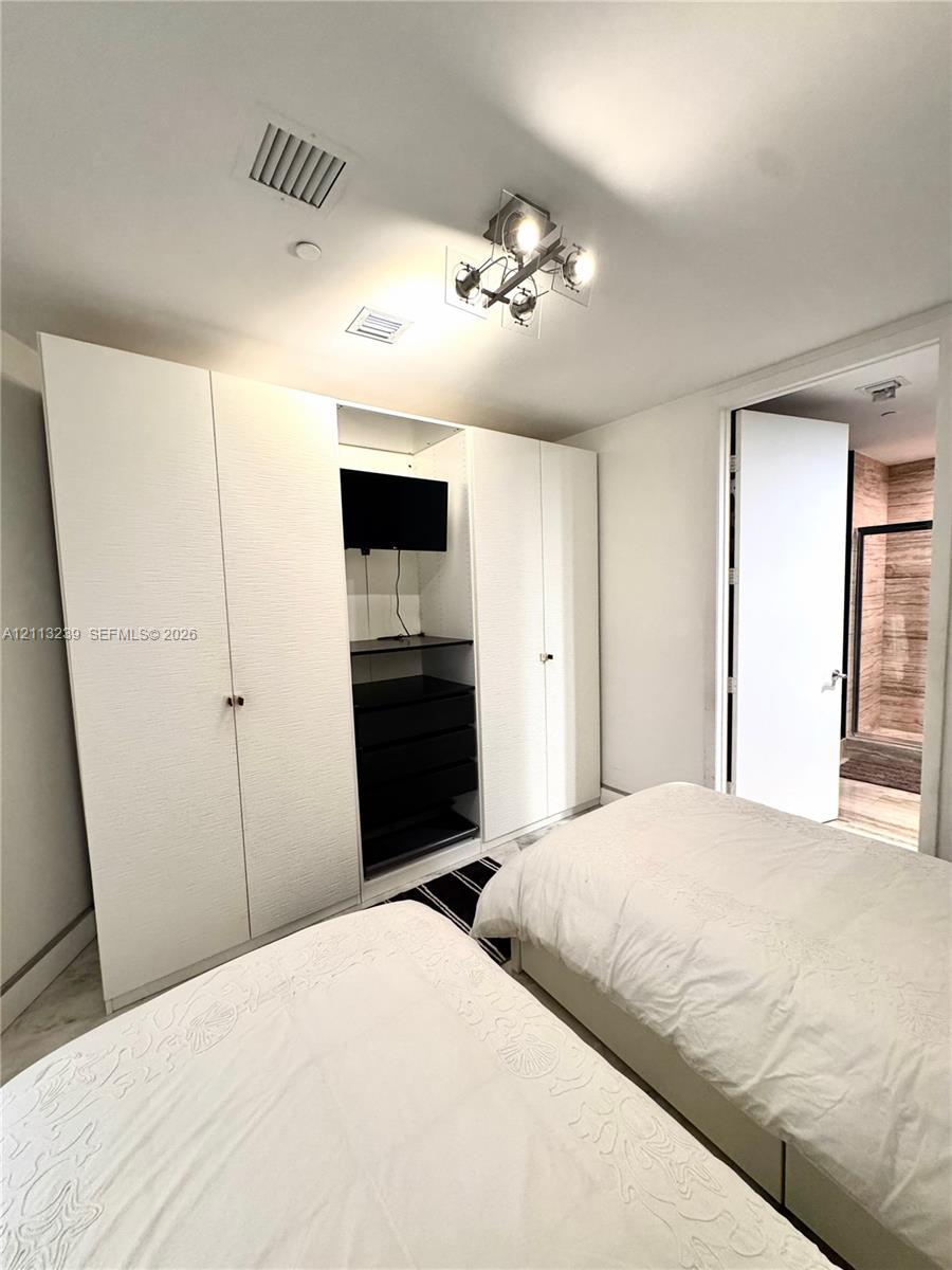 Built-in white cabinetry with integrated shelving and drawers, four-light modern ceiling fixture, and stone-finish flooring