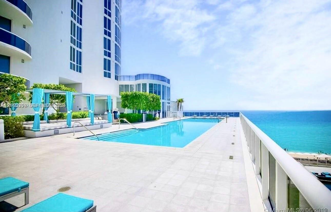 Outdoor swimming pool featuring a concrete sun deck, integrated steps, and metallic railings, set against an ocean backdrop