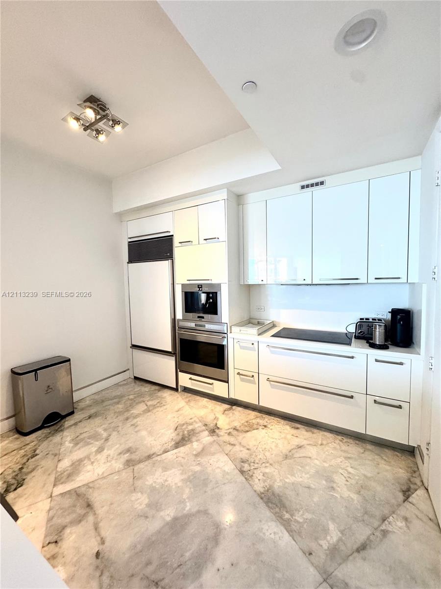 Sleek kitchen featuring high-gloss cabinetry, integrated stainless steel appliances, a built-in wall oven, a flat-surface cooktop, and large-format tile flooring