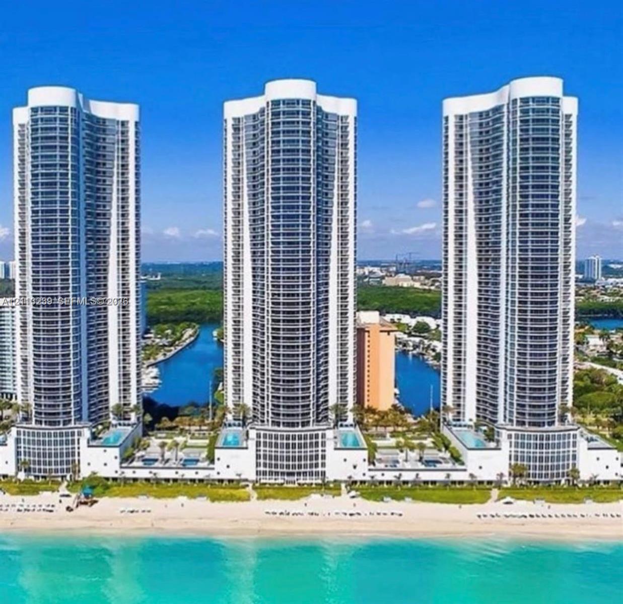 High-rise residential towers featuring glass-paneled balconies, exterior swimming pools, direct beachfront access, and water-front placement