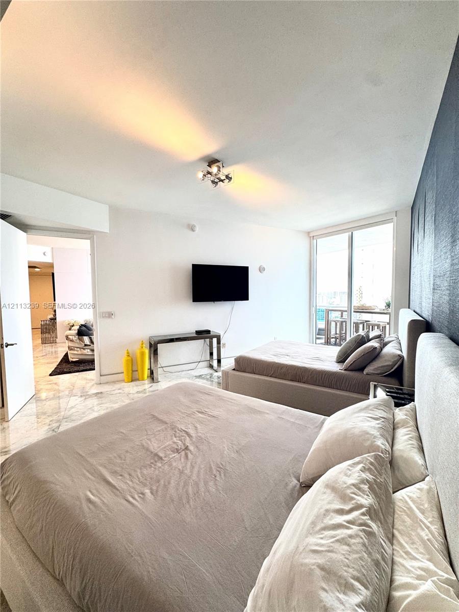 Polished stone flooring, floor-to-ceiling glass sliding doors, private balcony, and decorative dark accent wall