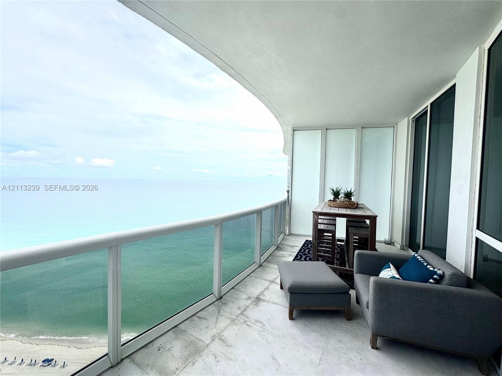 Curved private balcony featuring stone flooring, a glass-panel railing, and floor-to-ceiling glass sliding doors