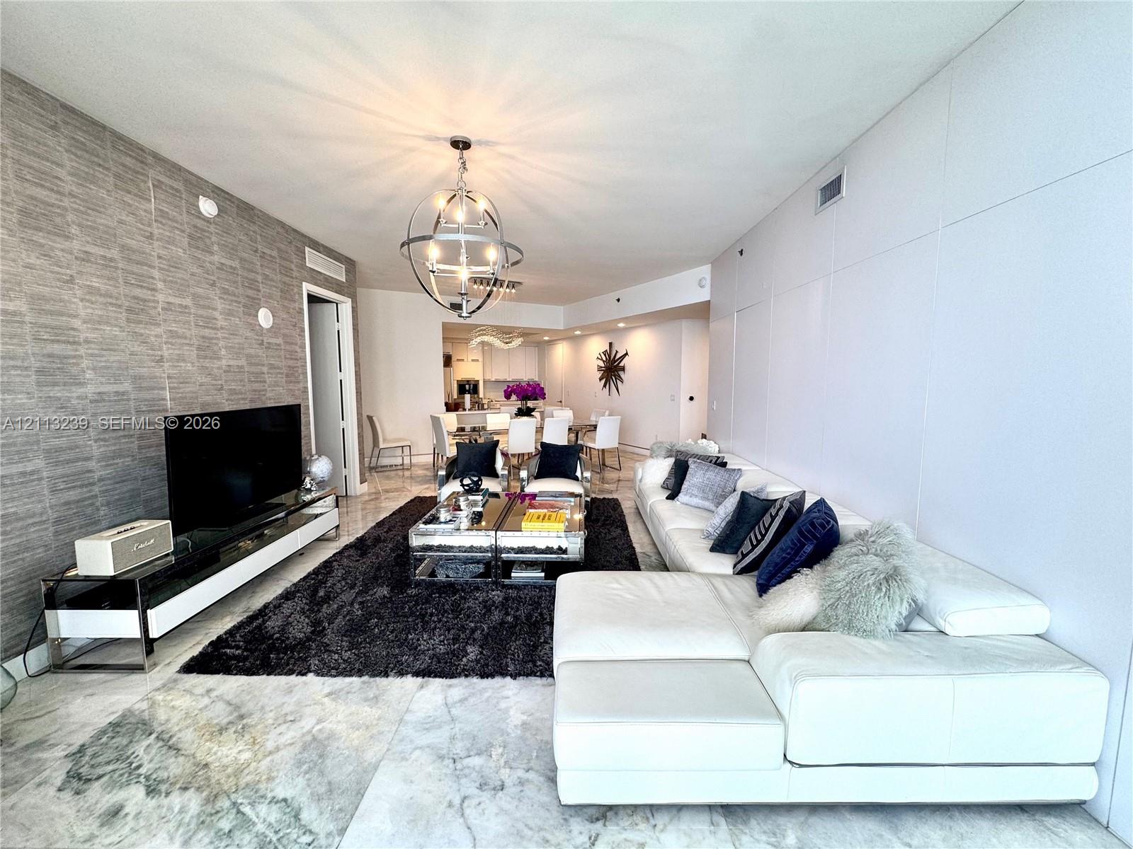 Living space featuring polished stone flooring, textured accent wall, and a spherical multi-light chandelier
