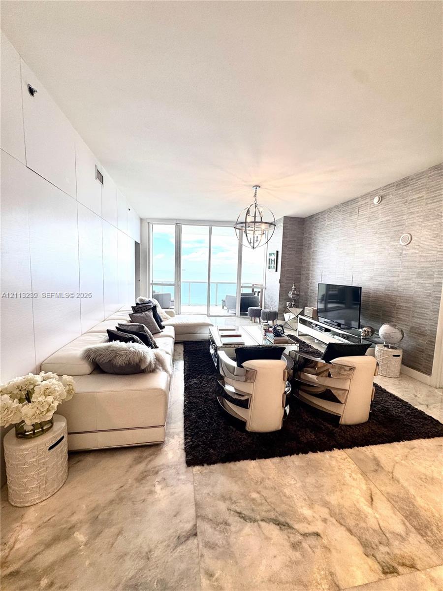 Living area featuring floor-to-ceiling glass paneling, stone tile flooring, a textured feature wall, and a contemporary spherical pendant light fixture